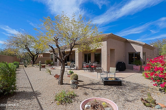 rear view of house featuring an outdoor fire pit, a patio area, fence, and stucco siding