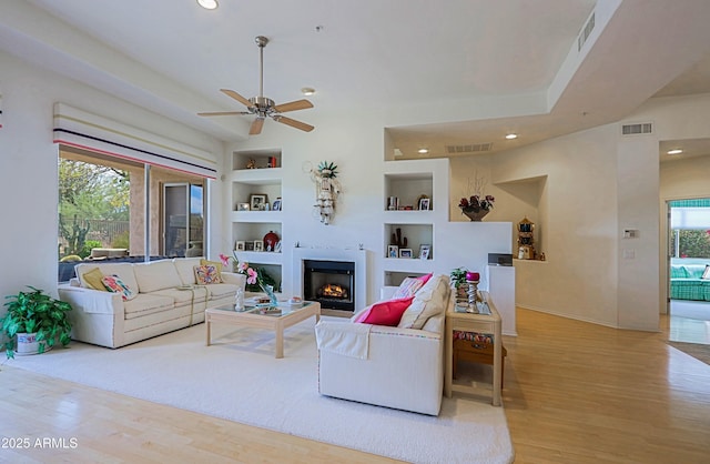 living room featuring built in shelves, wood finished floors, and visible vents