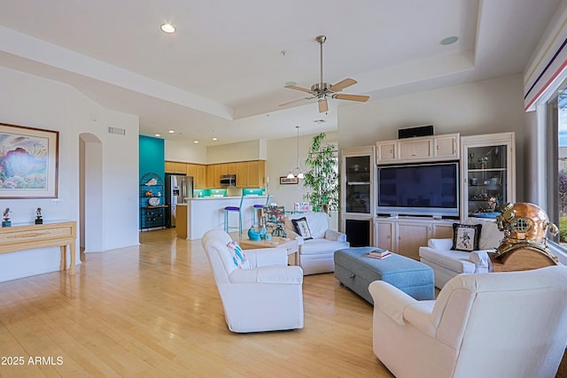 living room with arched walkways, light wood finished floors, a raised ceiling, and visible vents