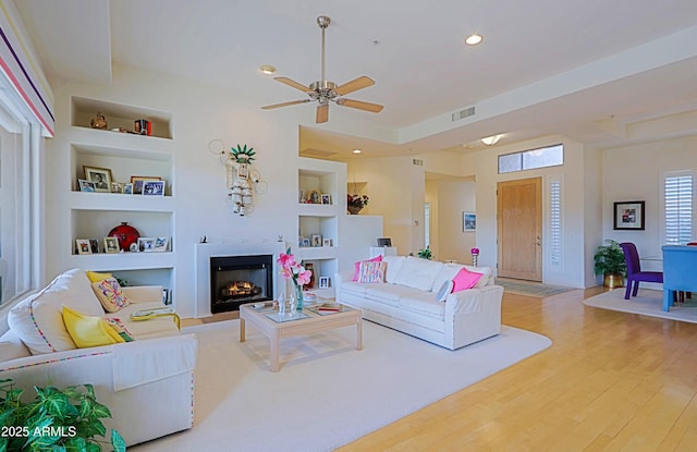 living room with visible vents, built in features, wood finished floors, a lit fireplace, and recessed lighting