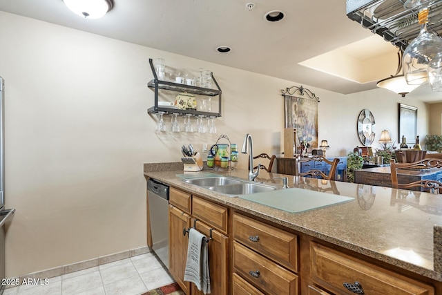 kitchen featuring light tile patterned floors, stone counters, stainless steel dishwasher, brown cabinetry, and a sink