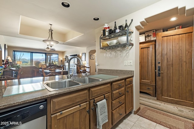 kitchen with brown cabinets, a sink, dark countertops, a raised ceiling, and dishwasher