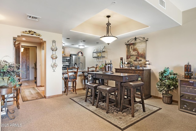 dining room with a raised ceiling, light colored carpet, visible vents, and baseboards