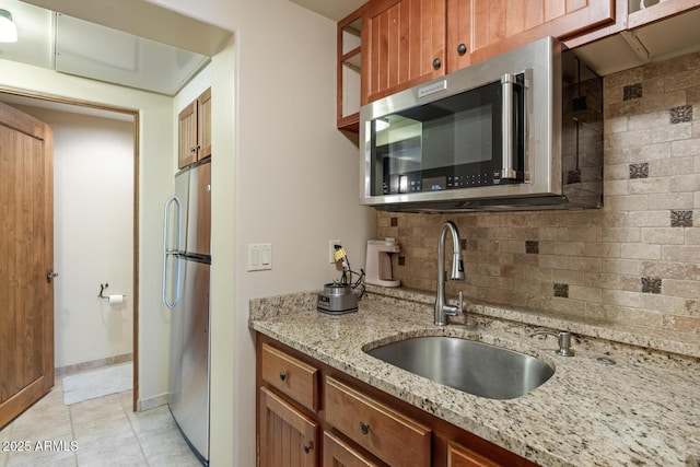 kitchen featuring light stone countertops, decorative backsplash, light tile patterned flooring, stainless steel appliances, and a sink