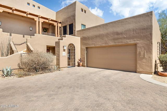 pueblo revival-style home with stucco siding, an attached garage, decorative driveway, and a balcony