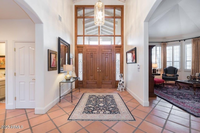 entryway with light tile patterned floors, visible vents, arched walkways, baseboards, and a towering ceiling