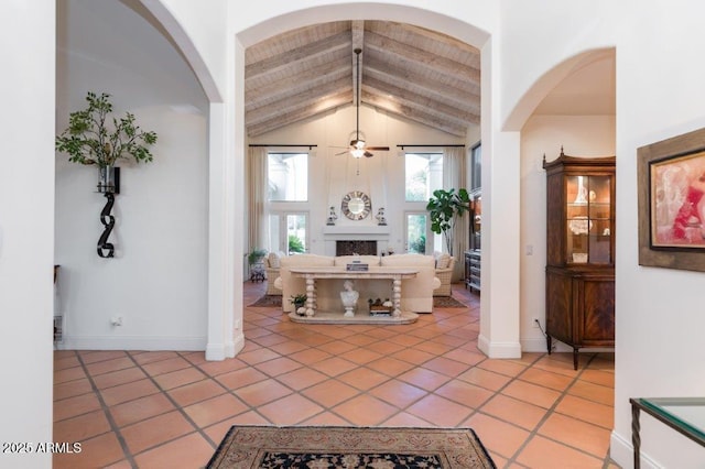 foyer featuring a fireplace, lofted ceiling with beams, a ceiling fan, light tile patterned flooring, and baseboards