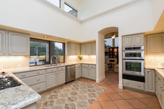 kitchen with light tile patterned floors, stainless steel appliances, tasteful backsplash, a sink, and light stone countertops