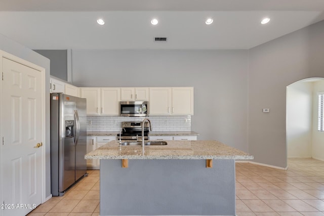 kitchen with light stone countertops, appliances with stainless steel finishes, white cabinetry, sink, and a kitchen island with sink