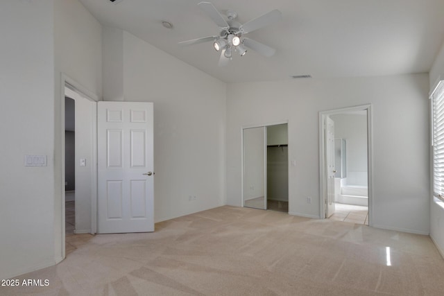 unfurnished bedroom with vaulted ceiling, a closet, light colored carpet, ceiling fan, and connected bathroom