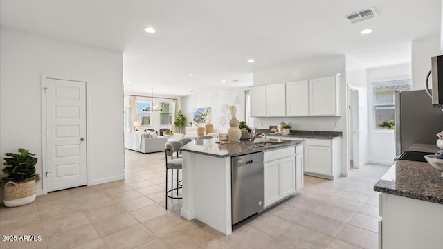 kitchen featuring an island with sink, appliances with stainless steel finishes, open floor plan, white cabinetry, and a sink