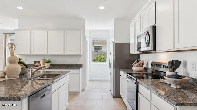 kitchen with light tile patterned floors, white cabinets, dark stone counters, stainless steel appliances, and a sink