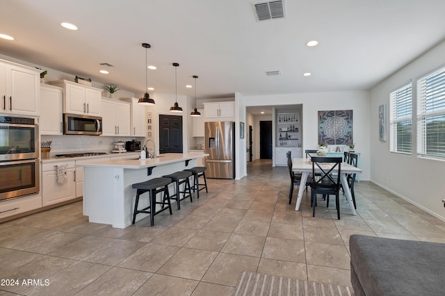 kitchen with sink, white cabinetry, decorative light fixtures, an island with sink, and stainless steel appliances