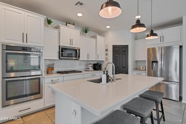 kitchen with stainless steel appliances, sink, white cabinets, and a kitchen island with sink