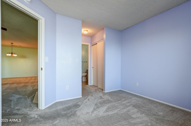 unfurnished bedroom featuring baseboards, carpet flooring, a textured ceiling, and a chandelier