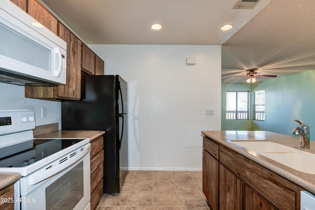 kitchen featuring visible vents, a ceiling fan, white appliances, brown cabinets, and a sink
