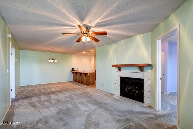 unfurnished living room with a textured ceiling, carpet, ceiling fan with notable chandelier, and a tile fireplace