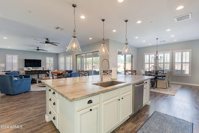 kitchen with light stone counters, stainless steel dishwasher, ceiling fan with notable chandelier, sink, and an island with sink