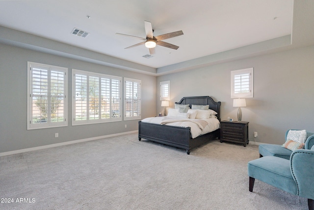 carpeted bedroom with a raised ceiling and ceiling fan