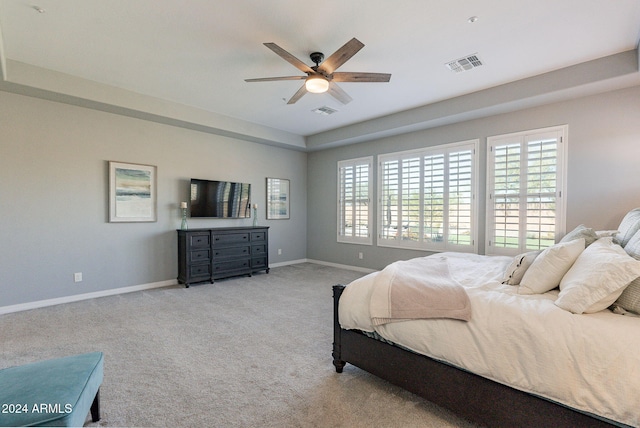 bedroom with a raised ceiling, multiple windows, ceiling fan, and light carpet