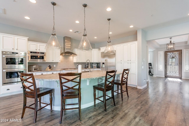 kitchen featuring a breakfast bar, pendant lighting, a spacious island, and wall chimney exhaust hood