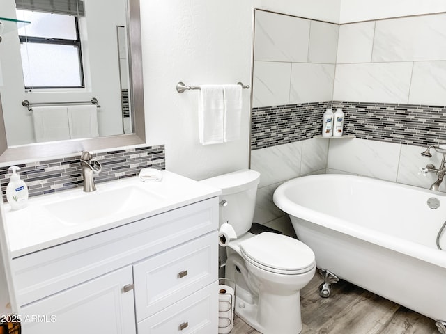 bathroom featuring backsplash, a tub to relax in, hardwood / wood-style flooring, vanity, and toilet