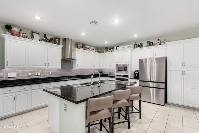 kitchen featuring a sink, appliances with stainless steel finishes, wall chimney exhaust hood, and white cabinetry