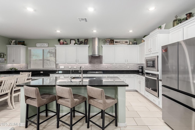 kitchen featuring visible vents, appliances with stainless steel finishes, wall chimney exhaust hood, and a breakfast bar