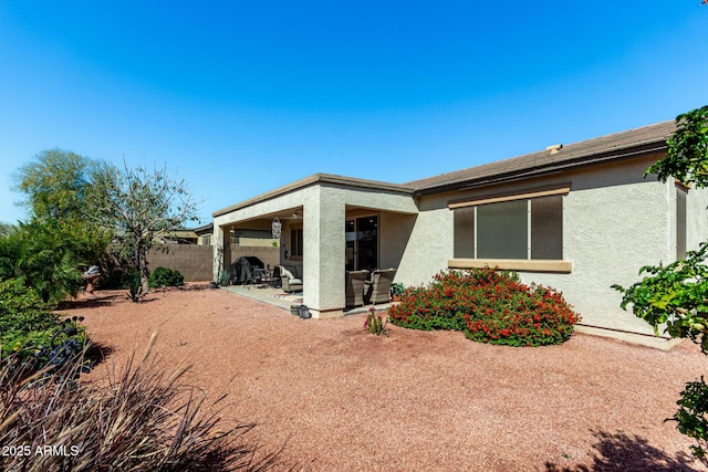 rear view of house featuring stucco siding, fence, and a patio area