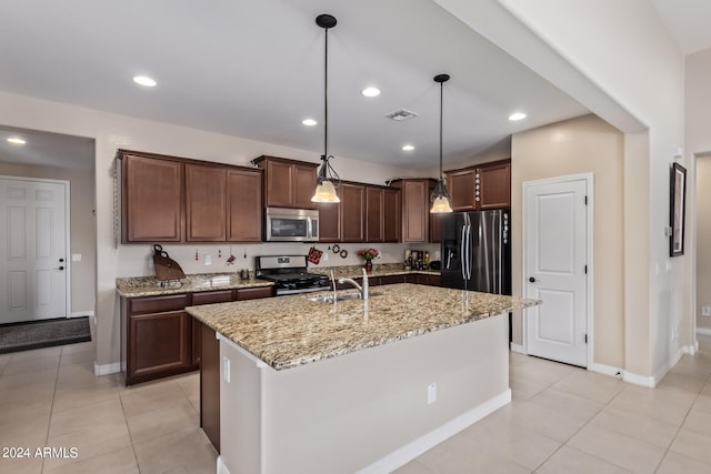 kitchen featuring light tile patterned floors, appliances with stainless steel finishes, an island with sink, light stone countertops, and decorative light fixtures