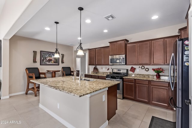 kitchen with light stone countertops, appliances with stainless steel finishes, sink, hanging light fixtures, and a kitchen island with sink