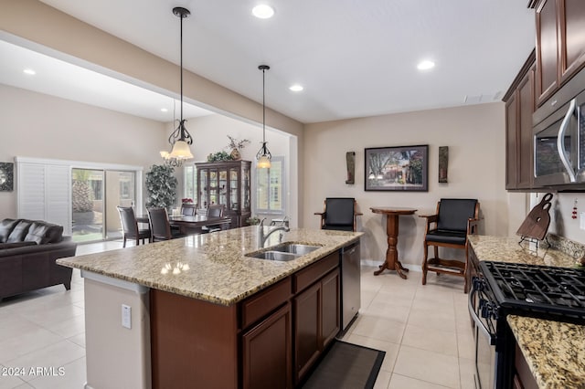 kitchen featuring appliances with stainless steel finishes, light tile patterned flooring, sink, decorative light fixtures, and a center island with sink