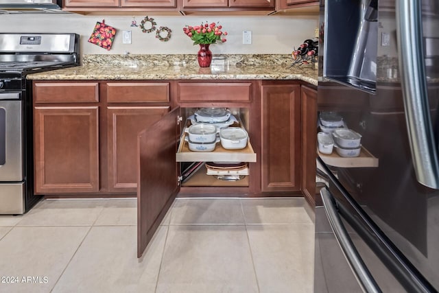 42915 W Kingfisher Dr, Maricopa, AZ 85138 - kitchen with fridge, light stone counters, brown cabinetry, stainless steel gas stove, and light tile patterned floors
