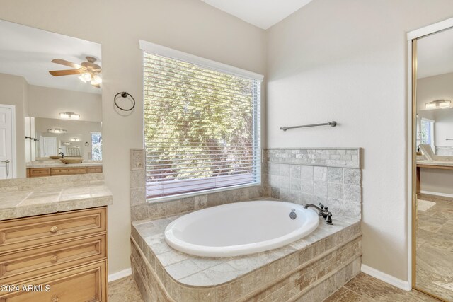 bathroom with tile patterned flooring, vanity, ceiling fan, and tiled tub