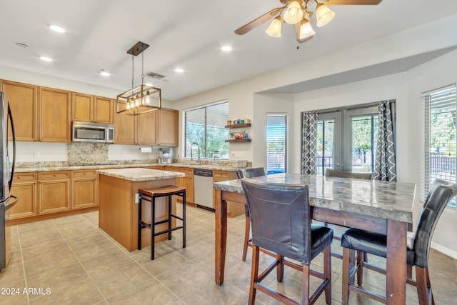 kitchen with french doors, a center island, light stone counters, decorative light fixtures, and appliances with stainless steel finishes