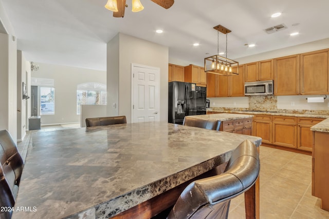 kitchen featuring ceiling fan, hanging light fixtures, light stone counters, a breakfast bar area, and black appliances