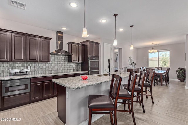 kitchen with a breakfast bar area, an island with sink, and wall chimney range hood