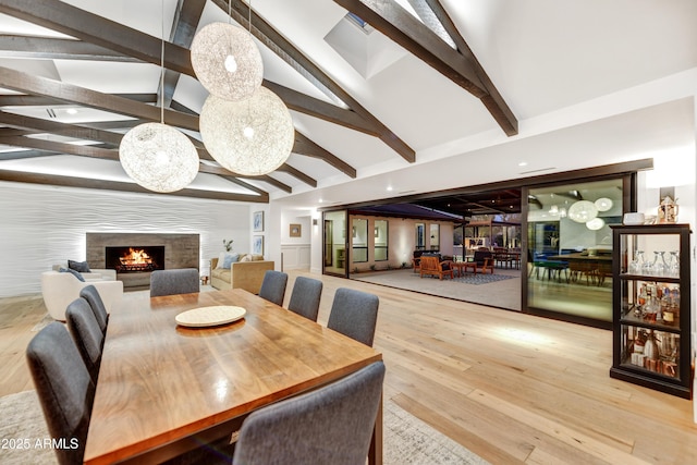 dining space featuring vaulted ceiling with beams, a lit fireplace, and wood finished floors