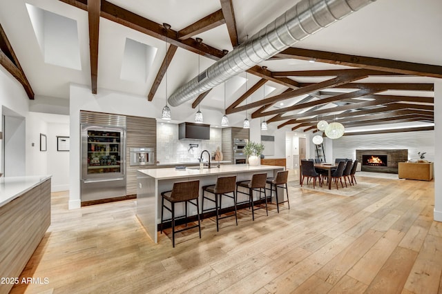 kitchen with light wood-type flooring, a breakfast bar, a sink, a high end fireplace, and light countertops