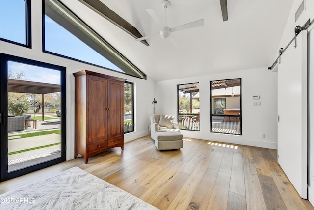 living area with a barn door, beamed ceiling, visible vents, and light wood finished floors