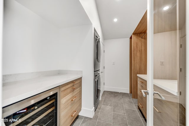 laundry room featuring beverage cooler, laundry area, recessed lighting, stacked washer and dryer, and dark tile patterned floors