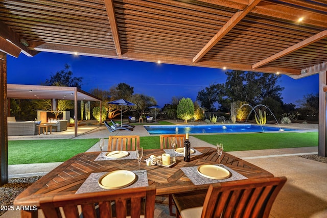 patio at night with an outdoor pool, a lawn, and outdoor dining space