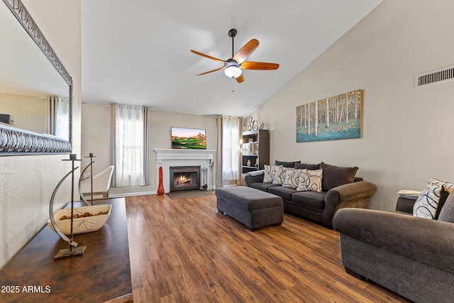 living room with visible vents, a ceiling fan, a fireplace with flush hearth, wood finished floors, and high vaulted ceiling