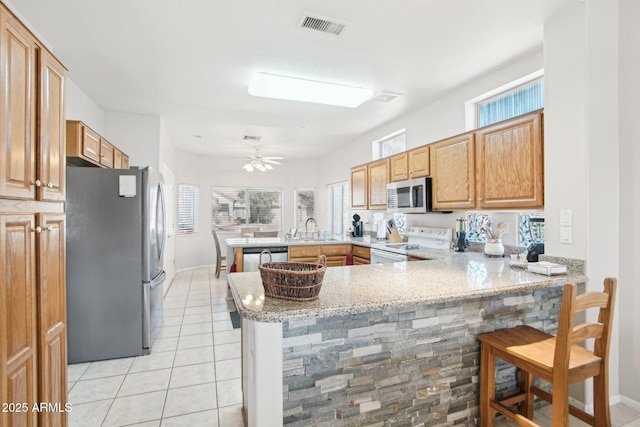 kitchen with sink, a breakfast bar area, appliances with stainless steel finishes, light stone counters, and kitchen peninsula