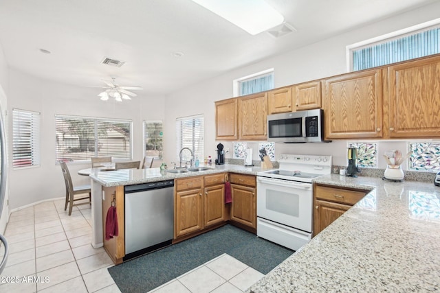 kitchen featuring sink, light tile patterned floors, light stone counters, kitchen peninsula, and stainless steel appliances