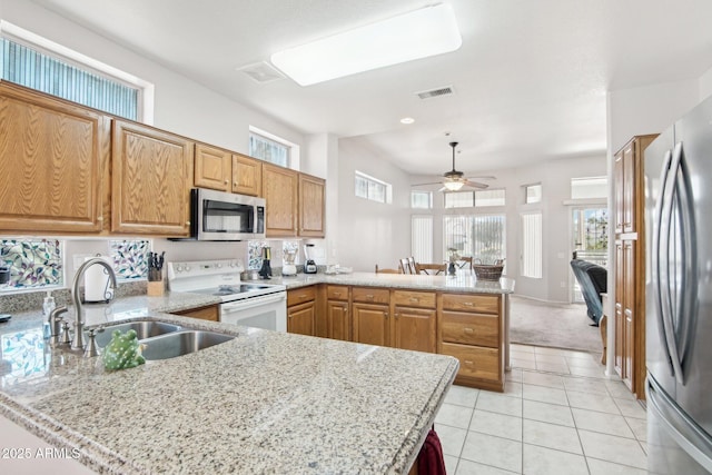 kitchen featuring light stone counters, stainless steel appliances, kitchen peninsula, and sink