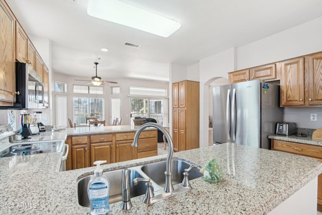 kitchen featuring sink, ceiling fan, stainless steel appliances, light stone countertops, and kitchen peninsula