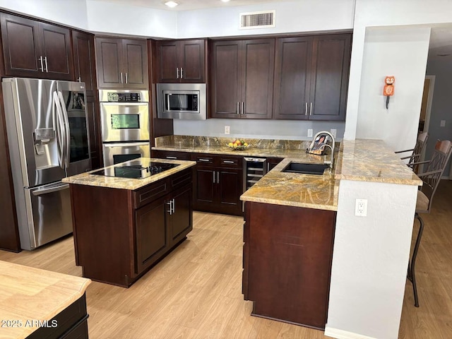 kitchen featuring visible vents, a sink, appliances with stainless steel finishes, light wood-style floors, and a peninsula