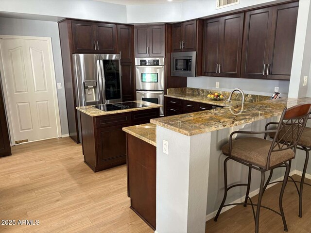 kitchen featuring a center island, light wood-type flooring, appliances with stainless steel finishes, dark brown cabinetry, and light stone countertops