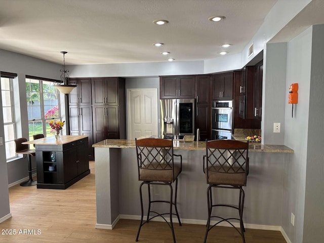 kitchen featuring light wood-style floors, dark brown cabinetry, a peninsula, visible vents, and stainless steel appliances
